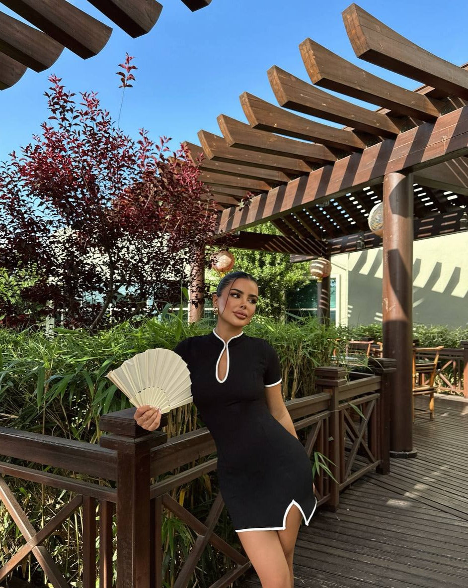 "Model posing on a wooden bridge, wearing the Black Tokyo Keyhole Mini Dress with white trim and keyhole neckline."