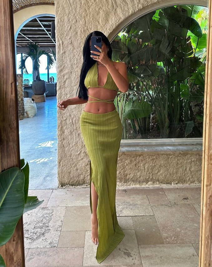 Model wearing the Tropical Chic Set in green, featuring a tie-up design and half-lined, zippered skirt, standing by a tropical resort."