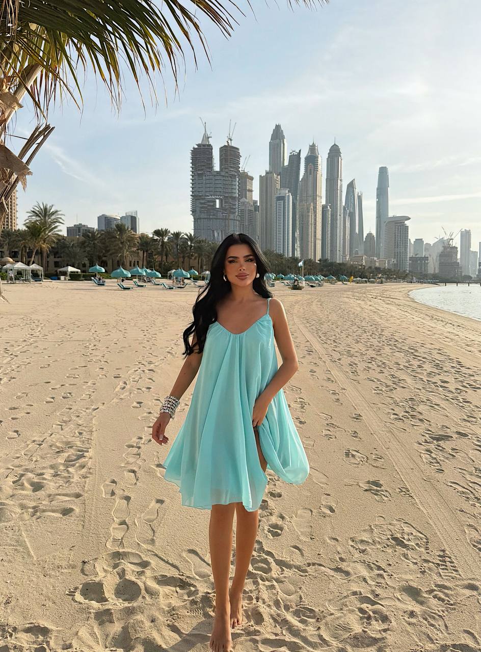 Woman in a light blue dress standing on a sandy beach with city skyline in the background